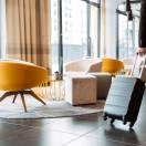Cropped photo of caucasian businessman wearing formal black suit walking with suitcase in hotel lobby